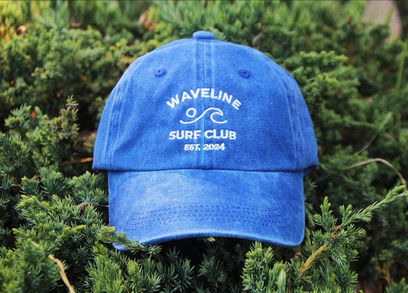 May include: A blue denim baseball cap with white embroidery that reads "Wavelline Surf Club Est. 2024".