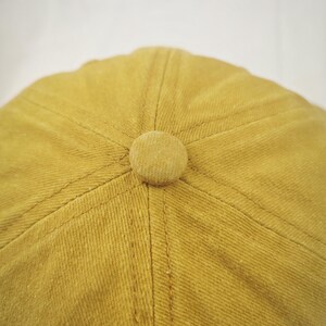 May include: A mustard yellow baseball cap with a fabric button on top.