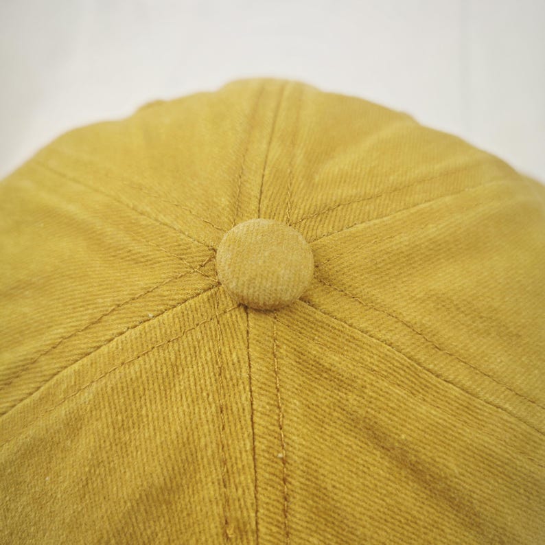 May include: A mustard yellow baseball cap with a fabric button on top.