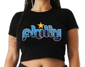 May include: A black cropped t-shirt with a blue and yellow graphic that says "philly" with a silhouette of the Philadelphia skyline.
