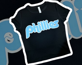 Op de afbeelding: Zwart T-shirt met een lichtblauwe "Phillies" afbeelding op de voorkant.