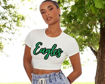 May include: White crop top with a green and black "Eagles" graphic. The top is made of a soft, stretchy fabric and has a relaxed fit.