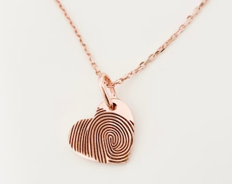 Puede incluir: Un collar de oro rosa con un colgante en forma de corazón con un diseño de huella digital.