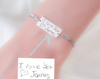 May include: Silver bracelet with a rectangular charm that says "I love you James" in handwritten script. The charm has a small heart drawn on it.