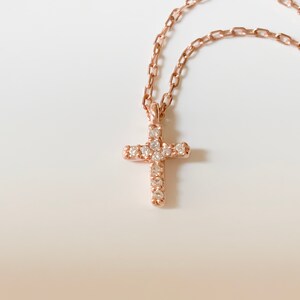Puede incluir: Un delicado collar de oro rosa con un peque&ntilde;o colgante de cruz brillante. La cruz est&aacute; adornada con piedras de circonita c&uacute;bica transparentes.