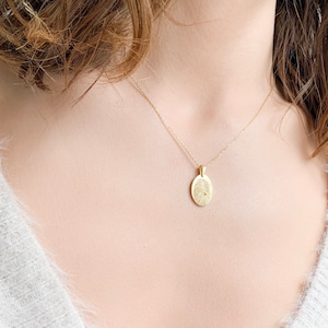 May include: A gold chain necklace with a small oval pendant featuring a detailed fingerprint design.