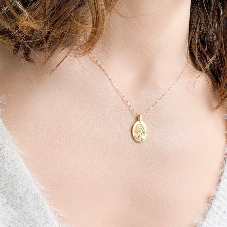 May include: A gold chain necklace with a small oval pendant featuring a detailed fingerprint design.