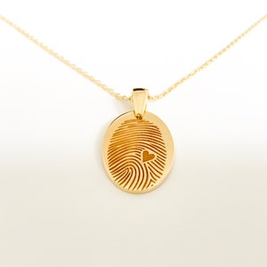 May include: A gold necklace with a pendant shaped like a fingerprint with a small heart cutout in the center.