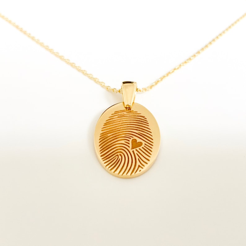 May include: A gold necklace with a pendant shaped like a fingerprint with a small heart cutout in the center.