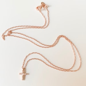 Puede incluir: Un delicado collar de cadena de oro rosa con un peque&ntilde;o colgante de cruz adornado con peque&ntilde;as piedras brillantes.