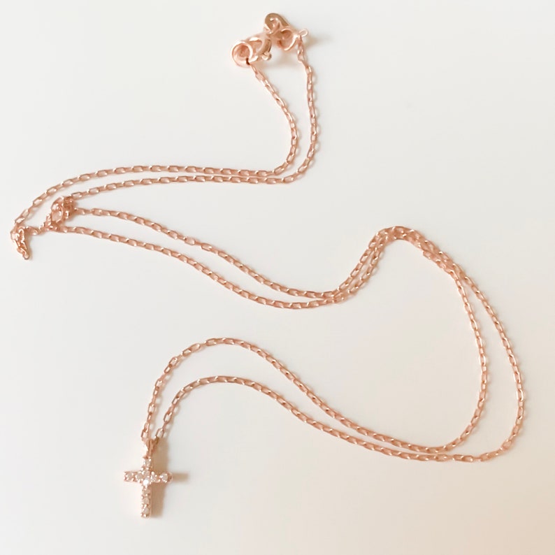 Puede incluir: Un delicado collar de cadena de oro rosa con un peque&ntilde;o colgante de cruz adornado con peque&ntilde;as piedras brillantes.