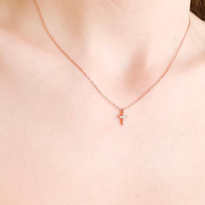 Puede incluir: Un delicado collar de cadena dorada con un peque&ntilde;o colgante de cruz brillante. La cruz est&aacute; adornada con peque&ntilde;as piedras transparentes.