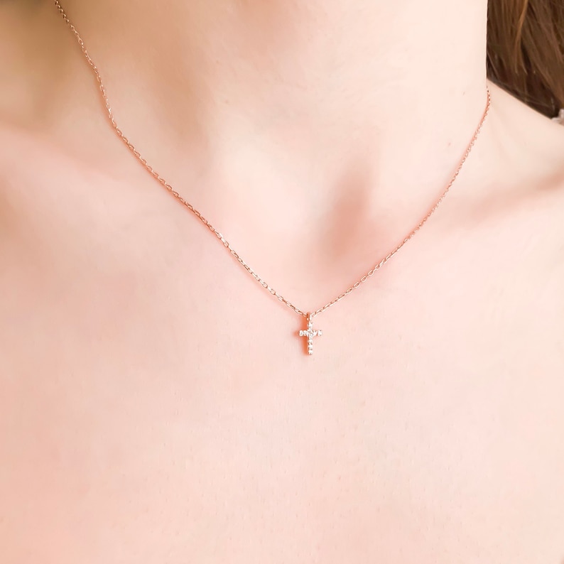 Puede incluir: Un delicado collar de oro con un peque&ntilde;o colgante de cruz brillante.