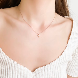 Puede incluir: Un delicado collar de cadena dorada con un peque&ntilde;o colgante de cruz brillante.