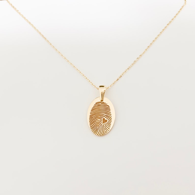 May include: A gold chain necklace with a pendant shaped like a fingerprint with a small heart cutout in the center.