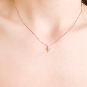 Puede incluir: Un delicado collar de cadena dorada con un peque&ntilde;o colgante de cruz brillante.