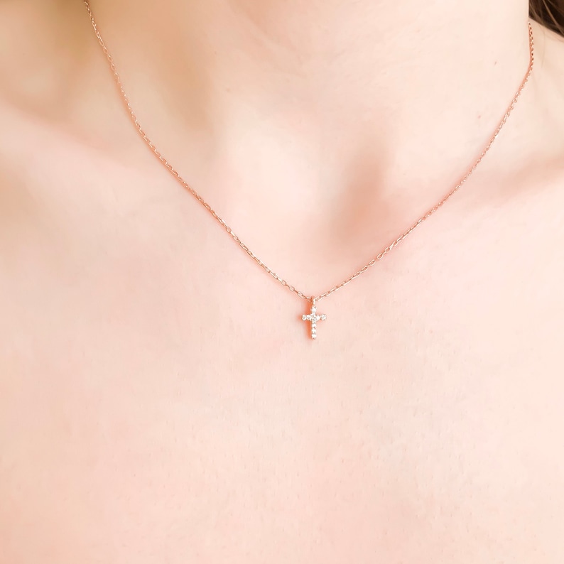 Puede incluir: Un delicado collar de cadena dorada con un peque&ntilde;o colgante de cruz brillante.