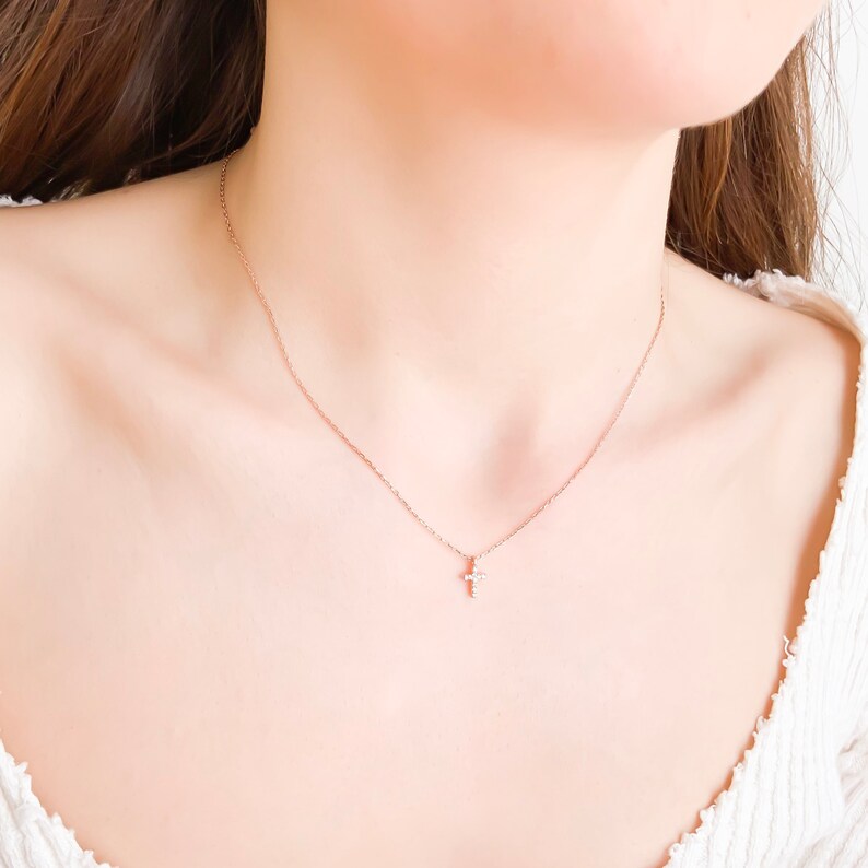 Puede incluir: Un delicado collar de cadena dorada con un peque&ntilde;o colgante de cruz brillante.