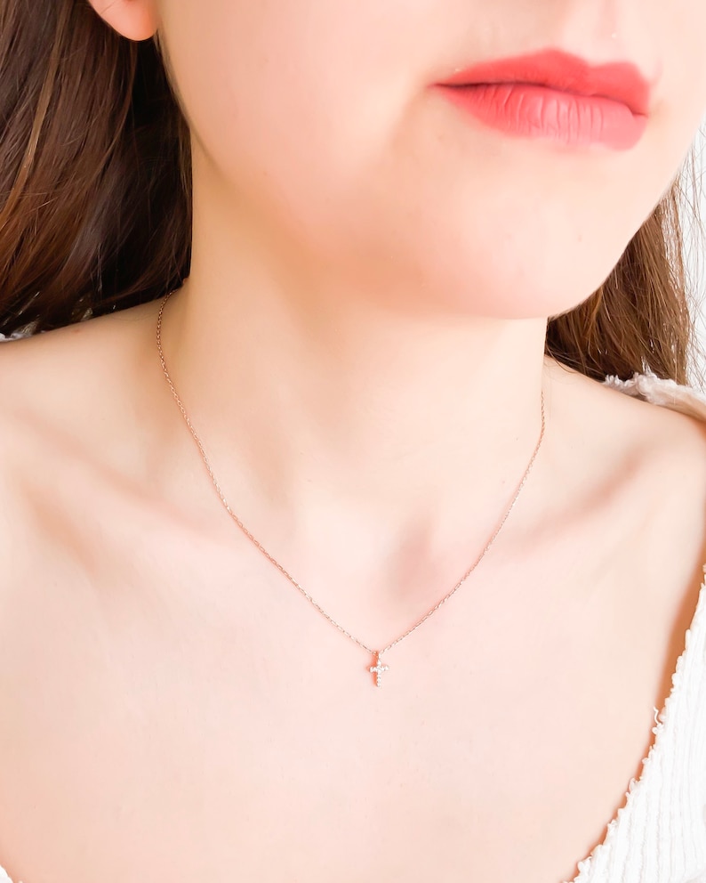 Puede incluir: Un delicado collar de cadena dorada con un peque&ntilde;o colgante de cruz brillante.