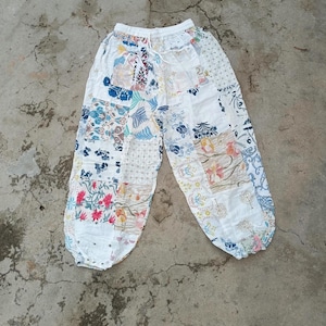 Könnte beinhalten: Patchwork-Hose mit weißem Grund und verschiedenen Blumen- und Pflanzenmustern in Blau-, Rosa-, Gelb- und Grüntönen. Die Hose verfügt über einen elastischen Bund mit Kordelzug sowie geraffte Beinabschlüsse an beiden Hosenbeinen.