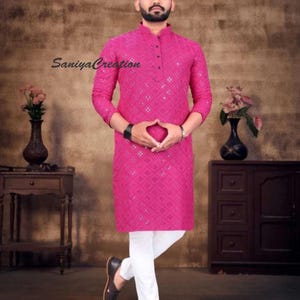 Pu&ograve; includere: Un kurta magenta con intricati specchi e maniche lunghe. &Egrave; abbinato a pantaloni bianchi e scarpe in pelle marrone scuro. L'immagine include il testo "Saniya Creation".