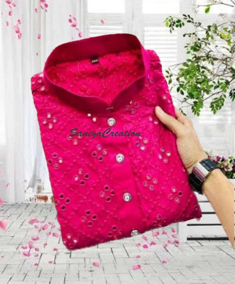 Pu&ograve; includere: Una camicia rosa acceso con colletto alla coreana. La camicia presenta un motivo ricamato dettagliato con piccoli specchietti. Il testo "Saniya Creation" &egrave; visibile sulla camicia.