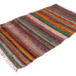 May include: A rectangular, striped rug with a variety of colors including red, green, orange, and brown. The rug has a fringed edge and is made of woven fabric. The rug's dimensions are not visible in the image.