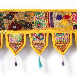 May include: A decorative yellow textile valance with embroidered patchwork designs in various colors. The valance has seven pendant-shaped tassels with colorful accents. The text "Saniya Creations" is visible on the left side.
