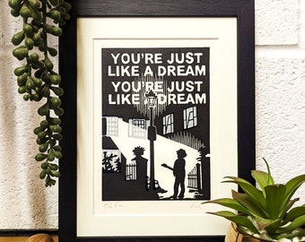 Op de afbeelding: Een zwart-witte ingelijste print van een straatbeeld met twee silhouetten. De tekst "YOU'RE JUST LIKE A DREAM YOU'RE JUST LIKE A DREAM" is in wit op een zwarte achtergrond gedrukt. De print is gesigneerd met "The Cure" en "Paul"