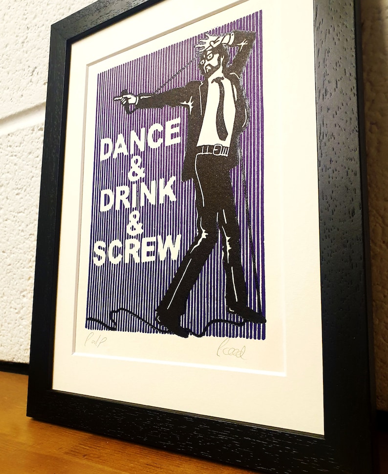 May include: Framed art print with a black frame. The print features a black and white illustration of a man in a suit with the words "DANCE & DRINK & SCREW" in white text on a purple striped background.