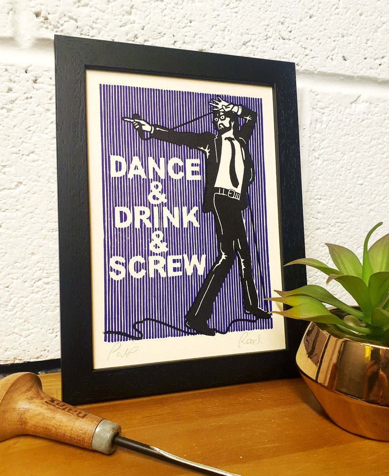 May include: Black framed art print with a man in a suit and the words "DANCE & DRINK & SCREW" in white text on a blue striped background. The artwork is signed by the artist.