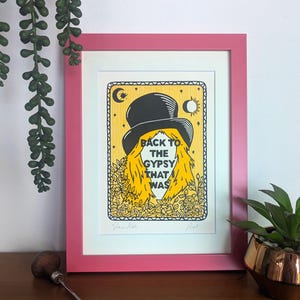May include: A framed art print with a pink border. The artwork features a yellow background with a woman wearing a black top hat. The text "BACK TO THE GYPSY THAT WAS" is displayed. The print is surrounded by yellow flowers.