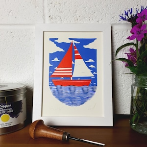 May include: A framed print of a red and white sailboat on a blue sea with white clouds. The print is signed in the bottom right corner.