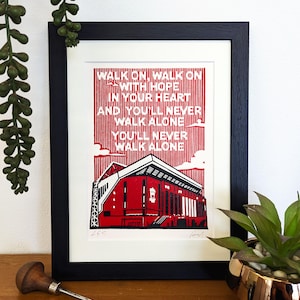 Könnte beinhalten: Ein gerahmter Druck einer roten und weißen Illustration eines Stadions mit den Texten "Walk on, walk on with hope in your heart and you'll never walk alone. You'll never walk alone." über dem Stadion.
