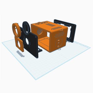May include: An exploded view of a 3D printed electronic enclosure featuring a bright orange main housing with ventilation holes, a black front panel with circular cutouts, and additional orange and black mounting components arranged in a sequence.