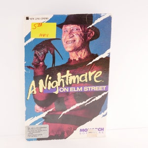 May include: A VHS tape case for the film "A Nightmare on Elm Street". The case features a red and black striped sweater, a brown fedora, and a menacing grin. The text "A Nightmare on Elm Street" is printed in white on a purple background.