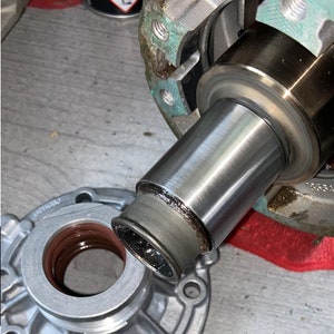 May include: Close-up of automotive components, featuring a cylindrical metal part with a dark ring and a silver housing. The parts suggest a mechanical assembly, possibly a differential or transmission.