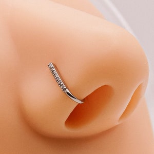 May include: A silver nose ring with a row of small clear stones. The ring is curved and has a small opening at the end.