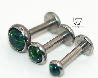 Puede incluir: Tres piezas de joyería corporal plateadas con piedras de ópalo verde. Las piezas son de diferentes tamaños, siendo la más grande la de la izquierda y la más pequeña la de la derecha.