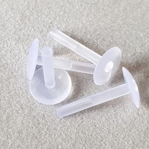 Op de afbeelding: Vier witte plastic oorbelruggen met een klein gaatje in het midden van elke rug. De ruggen zijn ontworpen om te worden gebruikt met oorbelsteentjes.