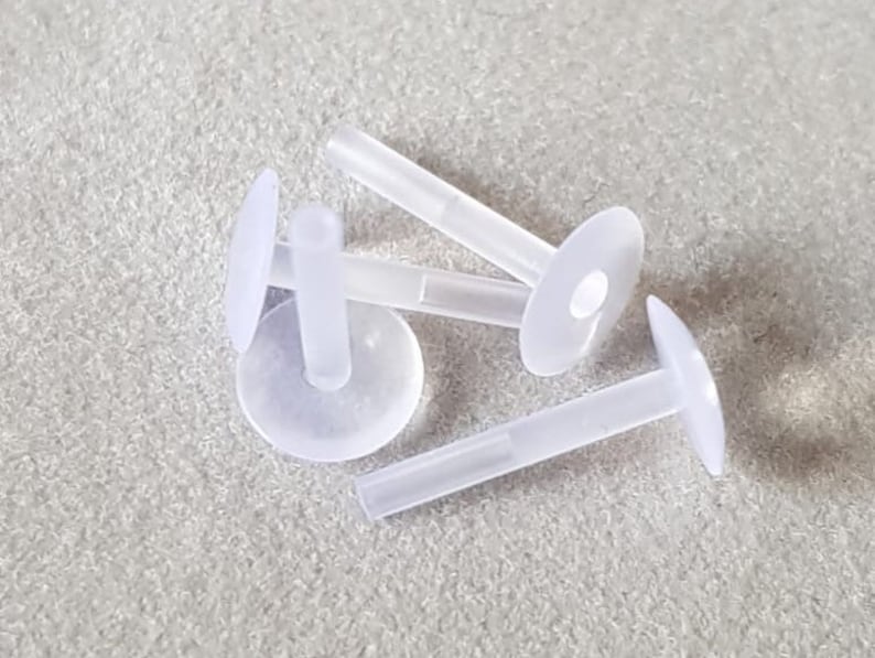 Op de afbeelding: Vier witte plastic oorbelruggen met een klein gaatje in het midden van elke rug. De ruggen zijn ontworpen om te worden gebruikt met oorbelsteentjes.