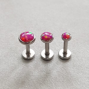 Puede incluir: Tres piezas de joyer&iacute;a corporal de plata con tapas de &oacute;palo rosa. Las piezas son de diferentes tama&ntilde;os, siendo la m&aacute;s grande a la izquierda y la m&aacute;s peque&ntilde;a a la derecha.