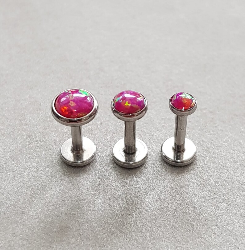 Puede incluir: Tres piezas de joyer&iacute;a corporal de plata con tapas de &oacute;palo rosa. Las piezas son de diferentes tama&ntilde;os, siendo la m&aacute;s grande a la izquierda y la m&aacute;s peque&ntilde;a a la derecha.