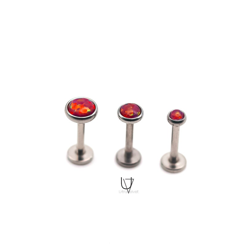 Puede incluir: Tres piezas de joyer&iacute;a corporal de plata con piedras de &oacute;palo rojo. Las piezas son de diferentes tama&ntilde;os, siendo la m&aacute;s grande a la izquierda y la m&aacute;s peque&ntilde;a a la derecha.