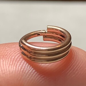 May include: A rose gold triple hoop earring. The hoop is made of three separate rings that are stacked on top of each other.