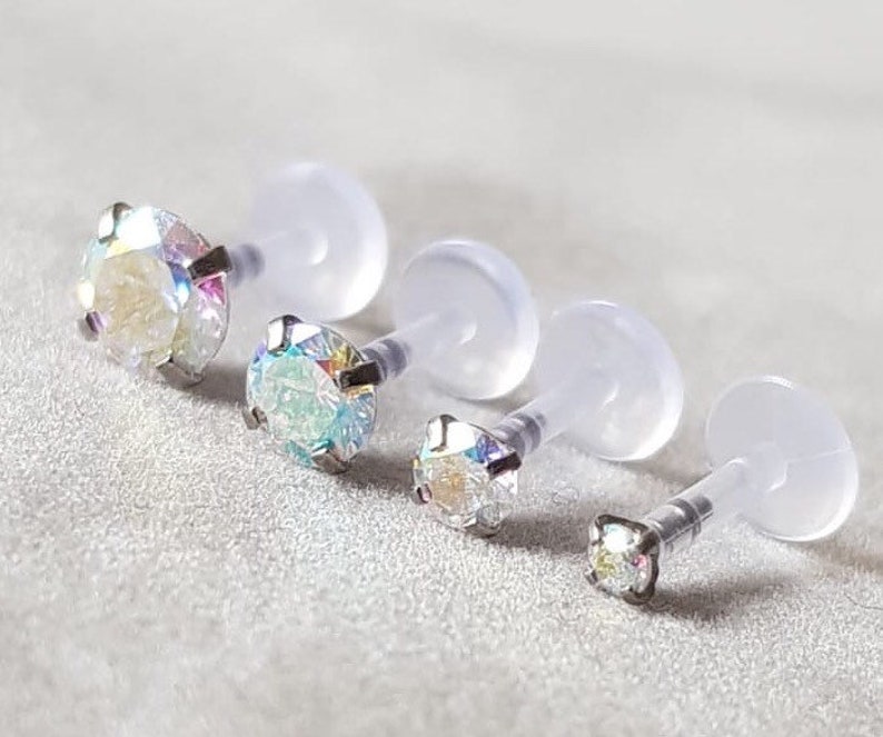 Op de afbeelding: Vier transparante lichaamssieraden van plastic met iriserende edelstenen. De stenen zijn rond, vierkant en ovaal.