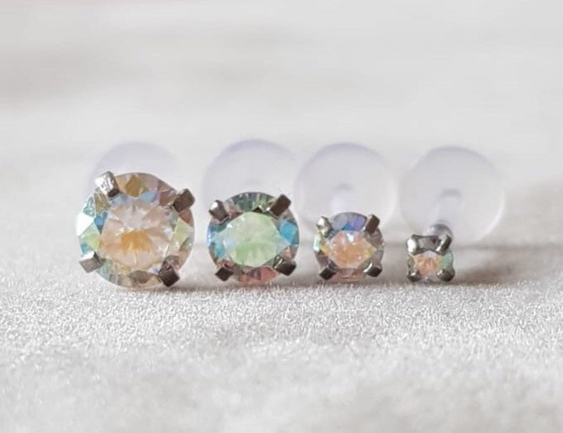 Op de afbeelding: Drie oorbel studs met iriserende edelstenen in verschillende maten. De oorbel studs zijn gezet in zilver en hebben een helder, facetgeslepen ontwerp.