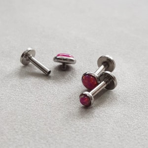 Puede incluir: Cuatro piezas de joyer&iacute;a corporal plateada con piedras de &oacute;palo rosa. Dos de las piezas son de estilo barra con un extremo de tornillo. Las otras dos piezas son tachuelas de respaldo plano.
