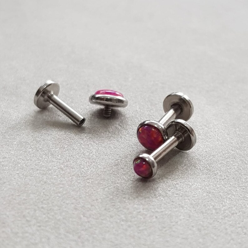 Puede incluir: Cuatro piezas de joyer&iacute;a corporal plateada con piedras de &oacute;palo rosa. Dos de las piezas son de estilo barra con un extremo de tornillo. Las otras dos piezas son tachuelas de respaldo plano.