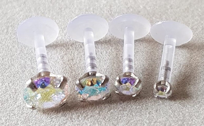 Op de afbeelding: Vier transparante lichaamssieraden van plastic met iriserende edelstenen. De stenen zijn veelkleurig met tinten blauw, groen en paars.